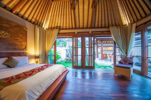 a bedroom with a bed in a room with windows at The Kampung Ubud Villa in Ubud