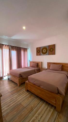 two beds in a room with wooden floors and windows at Cantika Guest House in Uluwatu