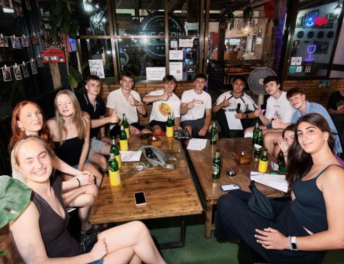 a group of people sitting around a table in a bar at The Cabin Backpackers Hostel & Bar in Chiang Mai