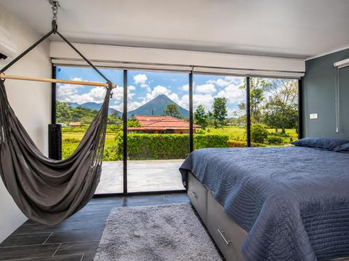 a bedroom with a hammock in front of a large window at Villa Los Perezosos - Private Jacuzzi & Arenal Volcano View - La Fortuna in Fortuna
