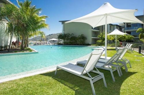 a group of chairs and an umbrella next to a swimming pool at Blue on Blue Apartment 912 in Nelly Bay