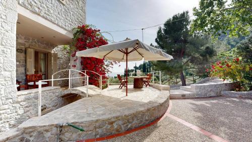 a patio with a table and an umbrella at Epidavros Villas - Elia Garden Retreat with Shared Pool in Nea Epidavros