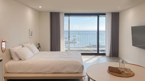 a bedroom with a bed and a table and a large window at Plott Archive Jeju in Jeju