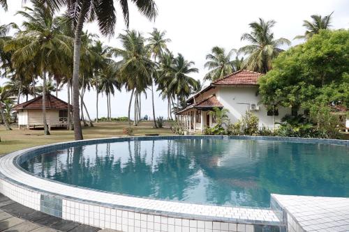 a swimming pool in front of a house with palm trees at Coconut Grove Beach Cabanas in Hungama