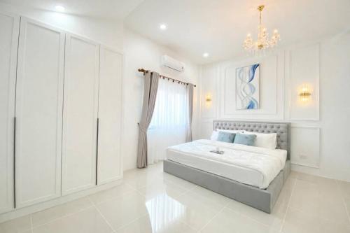 a white bedroom with a bed and a chandelier at Chill Sbai Villa Pattaya in Nong Prue