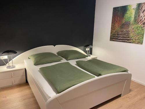 a white bed with green pillows in a bedroom at Ferienwohnung Haus Hahnfelsblick in Erfweiler