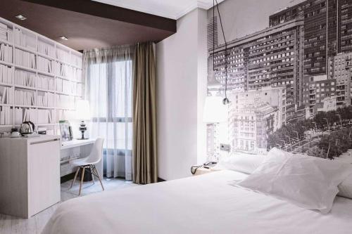 a bedroom with a white bed and a desk and a window at Hotel ILUNION Abando Bilbao in Bilbao