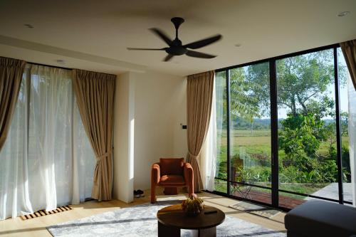 a living room with a ceiling fan and large windows at Padé Langkawi in Ulu Melaka