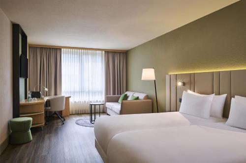 ein Hotelzimmer mit einem großen Bett und einem Schreibtisch in der Unterkunft NH Leipzig Messe in Leipzig