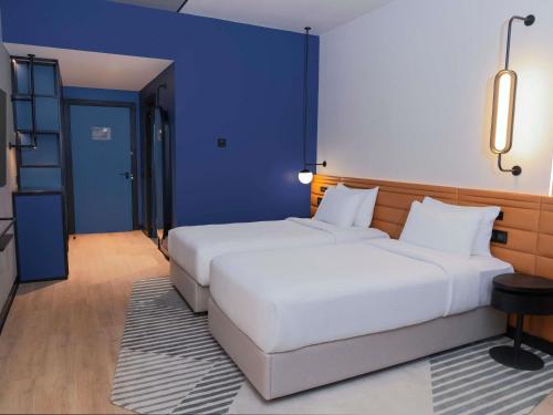 two white beds in a room with blue walls at Novotel Madinah in Medina