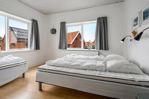 a white bedroom with a large bed with two windows at Activity House With Wellness Area-Sj700 in Thyborøn