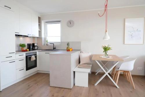 a kitchen with white cabinets and a table and a table and chairs at Meerblick D9 mit Balkon und Pool in Wangerland