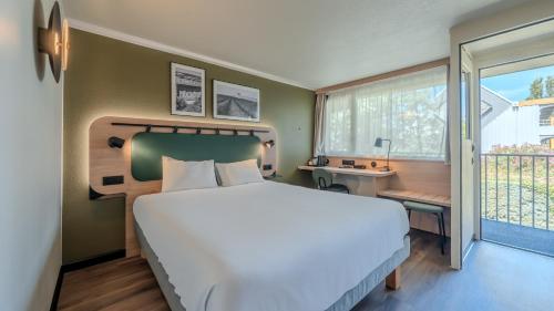 a bedroom with a bed and a desk and a window at Campanile NATURE - Orange in Orange