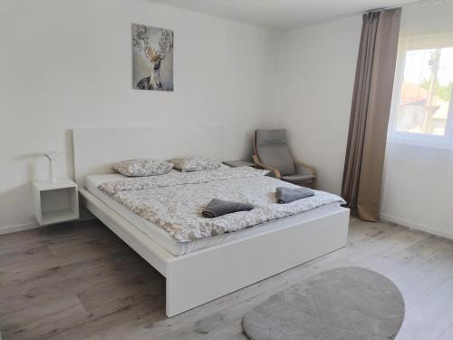 a white bedroom with a bed and a chair at Dömper Döme Apartman 1E in Balatonlelle