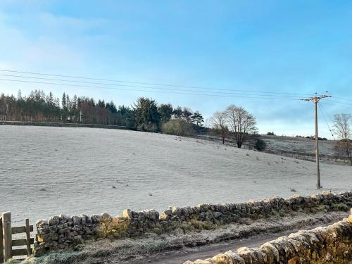 a snow covered field with a stone wall at Night Sky Cottage in Kielder
