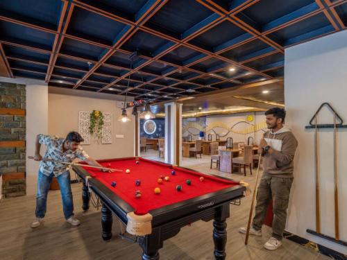 two men playing pool in a room with a pool table at The Hosteller Bam Bir in Bīr