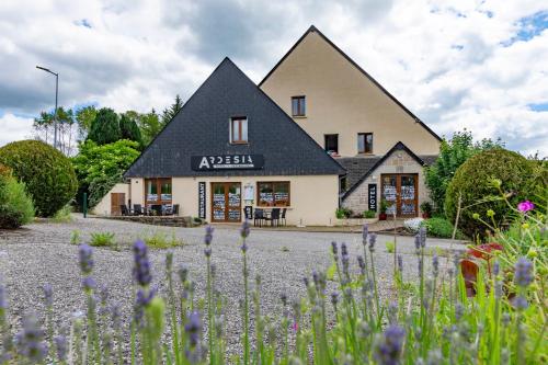 a house with a black roof and flowers in front of it at Hôtel Restaurant Ardesia in Peyrelevade