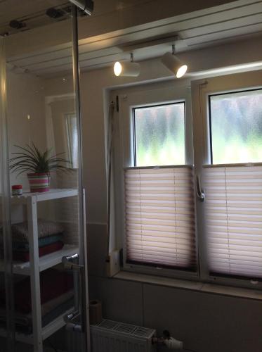 two windows with blinds in a bathroom with a mirror at Terassenwohnung in Starzach