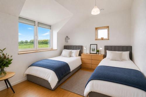 two beds in a bedroom with two windows at Brook Lodge Farm in Uckfield