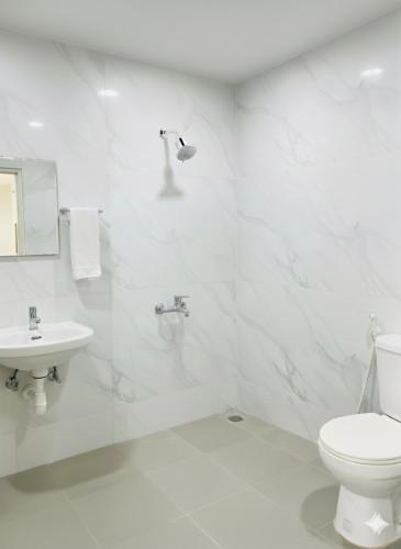 a white bathroom with a toilet and a sink at Forum Stay in Mysore