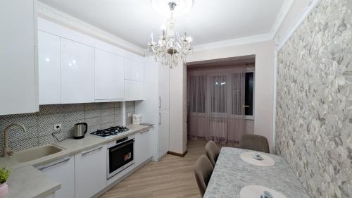 a kitchen with white cabinets and a table and a chandelier at Аэропорт Комфорт in Chişinău