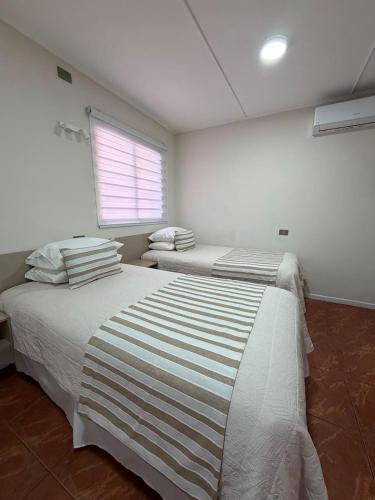 two beds in a white room with a window at Hotel Frontera in Antofagasta