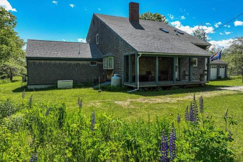 a house with a yard with purple flowers in front of it at Waterfront stay with scenic deck, grill, smart TVs, shore access - dog-friendly in Penobscot