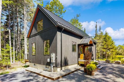 a black tiny house in the woods at Charming New Home with Hot Tub, Spacious Deck, Gas Grill, WiFi, and Washer/Dryer in Boothbay