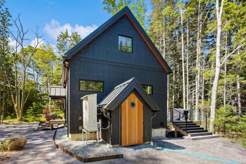 a black tiny house in the woods at Charming New Home with Hot Tub, Spacious Deck, Gas Grill, WiFi, and Washer/Dryer in Boothbay