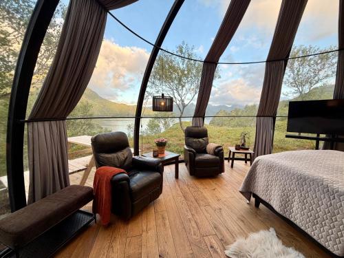 a room with a bed and chairs and a large window at Lofoten Aurora Dome in Hanøya