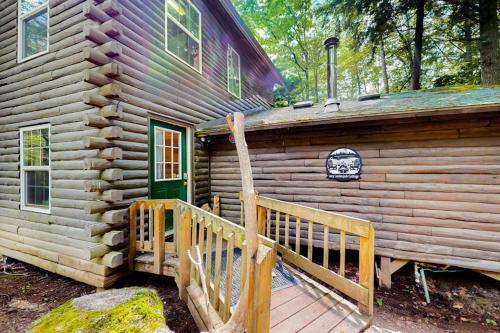 a log cabin with a wooden porch and a green door at The Cottage - Peaceful 32-Acre Lakefront Getaway - Canoe, Firepit & Big Deck in Franklin
