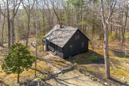 an aerial view of a black house in the woods at Renovated woodland home with lovely deck & firepit - minutes to Swan Lake in Swanville