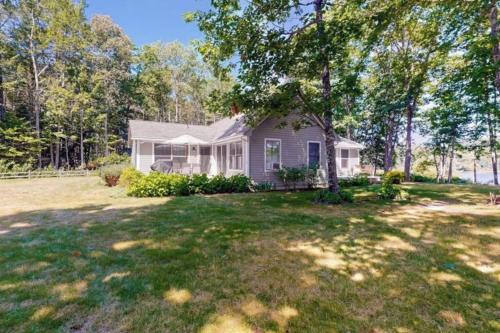 a white house with a tree in a yard at Secluded lakefront home with patio & firepit, fast WiFi, wood stove & W/D in Ellsworth