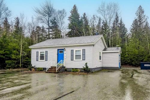 a white house with a blue door in a parking lot at Open layout Maine cottage with washer/dryer & grill - dog-friendly in Gouldsboro