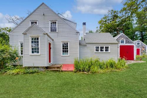 an old house with a red door in a yard at Historic riverfront home with boathouse & private dock - dogs OK in Boothbay