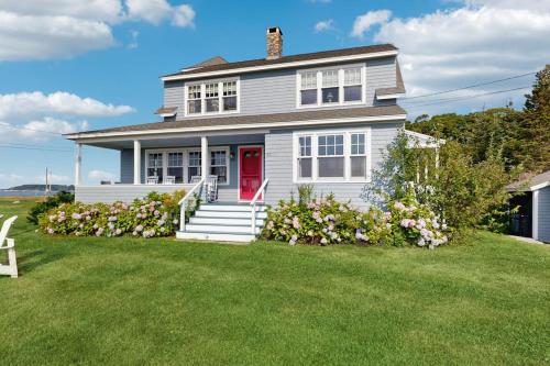 a white house with a red door on a lawn at Oceanfront home incredible ocean views, deck & location in Boothbay