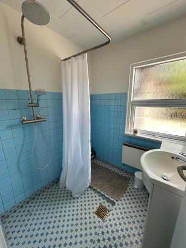 a blue tiled bathroom with a shower and a sink at Sommerhus i Hals in Hals