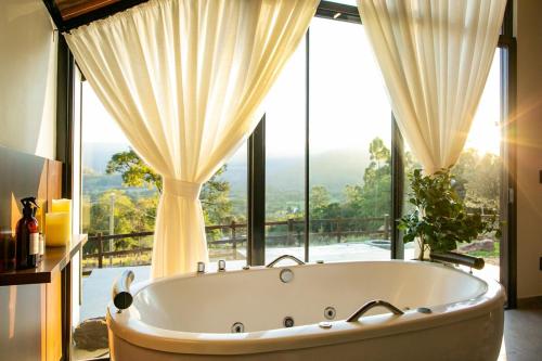 a bath tub in a bathroom with a large window at Encosta do Café - Chalé Oliveira in Itati