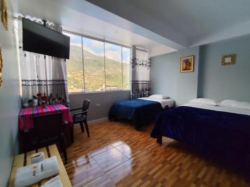 a bedroom with two beds and a table and a window at Hotel El Sol de Carhuaz in Carhuaz