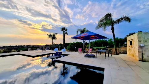 a pool with chairs and a blue umbrella and palm trees at Dreaming Polignano in San Vito