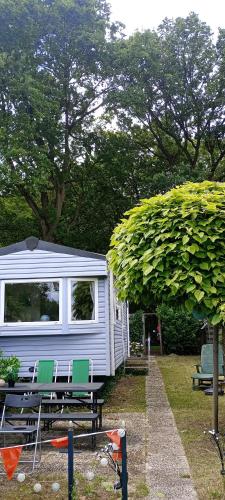 a caravan with two chairs and a table and a tree at Twee slaapkamer stacaravan met vissteiger in Hengelo