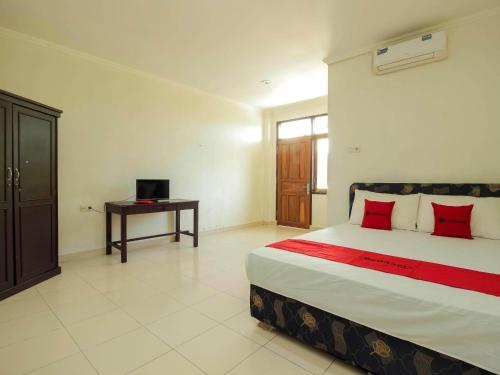 a bedroom with a bed with red pillows and a desk at RedDoorz @ Malalayang Manado in Manado
