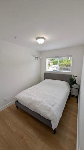 a white bedroom with a bed and a window at Bright & Cozy Garden Level Suite in North Vancouver