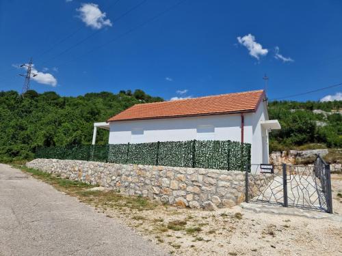 a house behind a stone wall next to a road at Vuković house - Lake View & Nature in Kuside