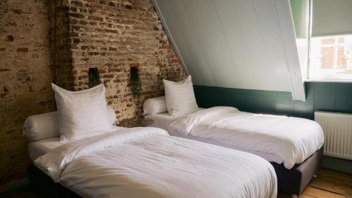 two beds with white sheets in a room with a brick wall at Bed en kerk monumentale 2 slaapkamer woning in Hoorn