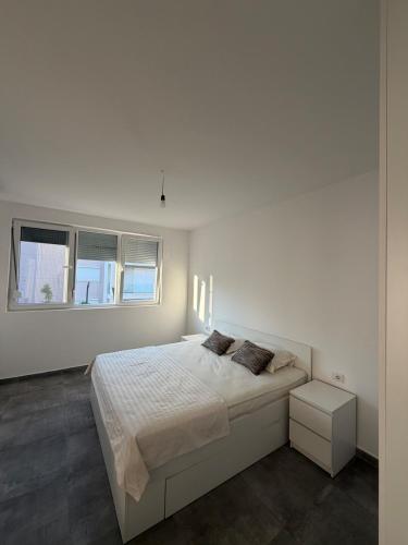a white bedroom with a large bed and two windows at BR Tale in Lezhë