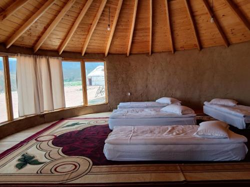 a row of four beds in a room with windows at Asman Tör Yurt Camp in Tong