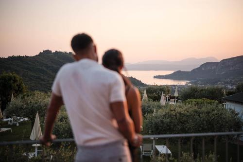 a man and a woman standing on a balcony looking at the ocean at Hotel Boffenigo - The Golden Hour in Costermano