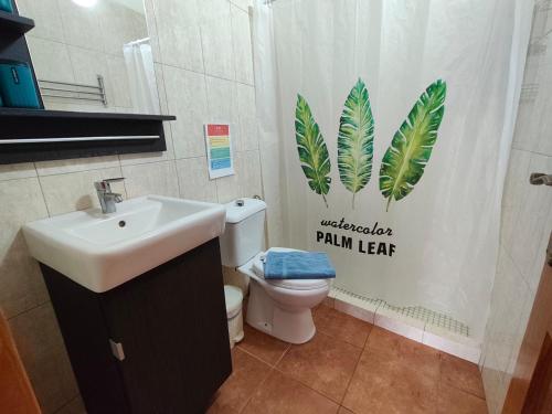 a bathroom with a sink and a toilet with a palm leaf shower curtain at Estudio Mary Espectaculares Vistas al Mar in Los Llanillos