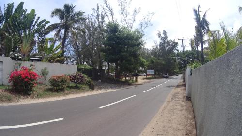 an empty road with a fence and palm trees at Allamanda Apartments - 100m Bain Boeuf Beach in Bain Boeuf